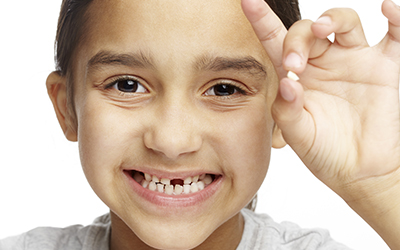 A young child holding up a missing tooth